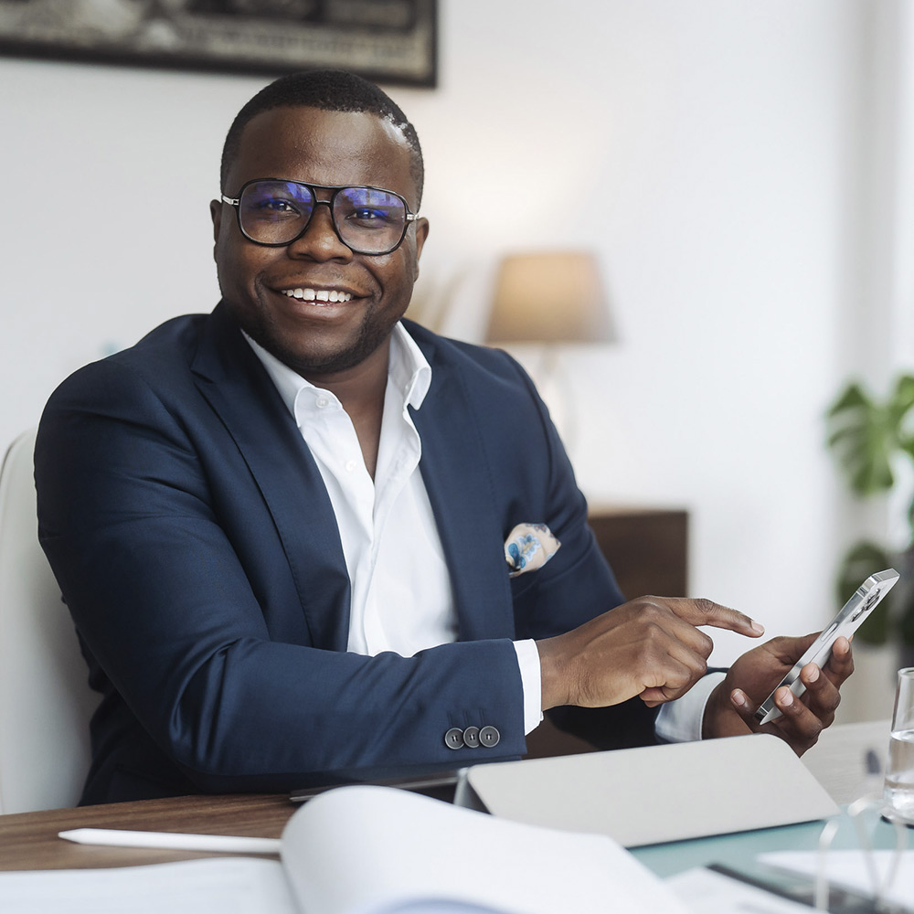 Alvin Lisebushira mit Brille, lächelnd, ein Telefon in der Hand.