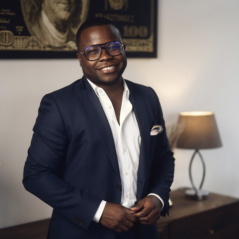 Alvin Lisebushira im dunklen Anzug, lächelnd, in einem Wohnraum.