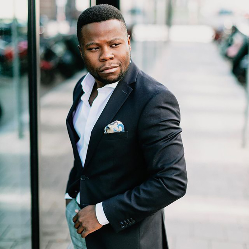 Alvin Lisebushira im dunklen Anzug mit Einstecktuch, in einem hellen Treppenhaus.