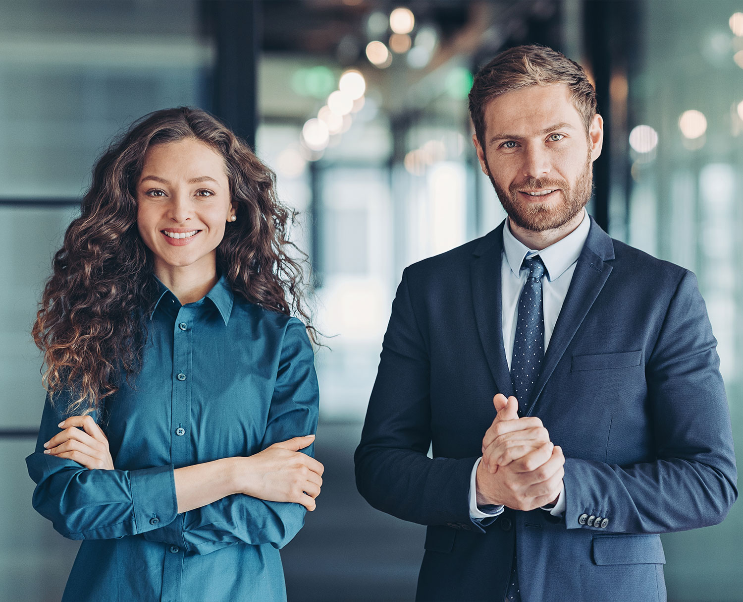 Eine Frau und ein Mann in Businesskleidung stehen nebeneinander und blicken in die Kamera.